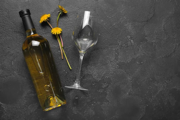Bottle and glass of dandelion wine on black background