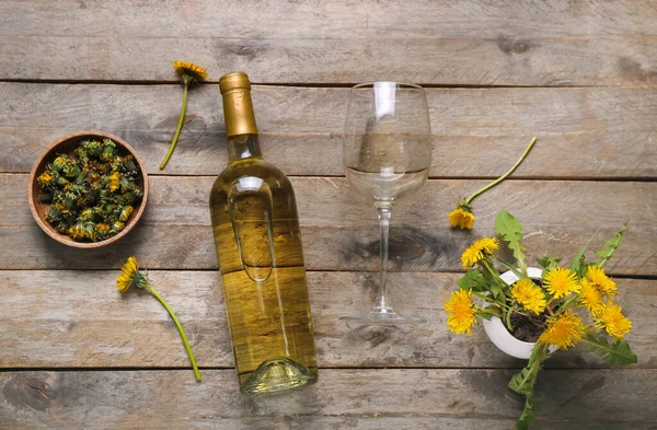 Bottle and glass of dandelion wine on wooden background