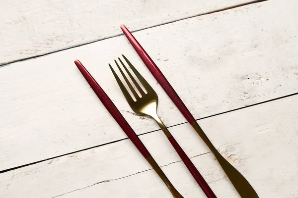 stock image Golden fork and knives with red handles on white wooden background