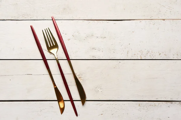 金色のフォークと白い木製の背景に赤いハンドルのナイフ — ストック写真