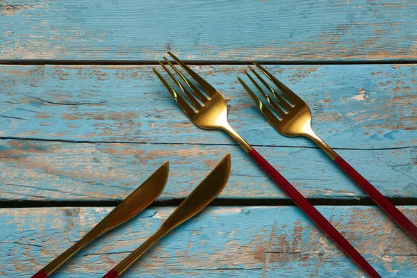 青い木製の背景に赤いハンドル付きの黄金のフォークとナイフ — ストック写真