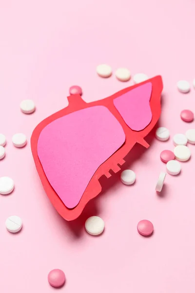 Paper liver with pills on pink background