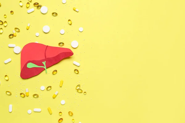 Red paper liver with pills on yellow background