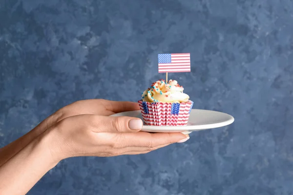 プレート おいしい愛国的なカップケーキとグランジブルーの壁の近くにアメリカのフラグを持つ女性の手 アメリカ独立記念日 — ストック写真