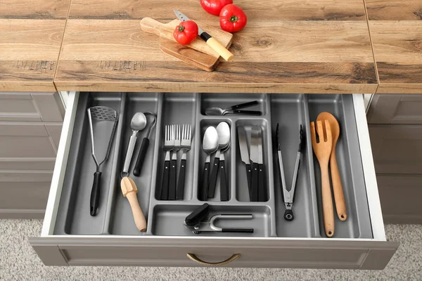 Open kitchen drawer with different silver cutlery and fresh tomatoes on board