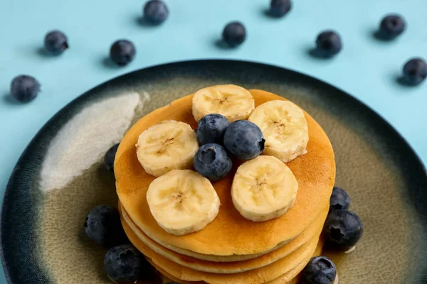 Plate with sweet pancakes, banana and blueberry on blue background, closeup