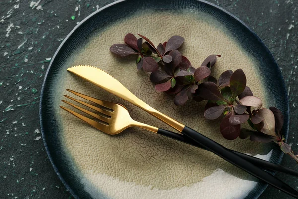 stock image Golden fork and knife with barberry twig in plate on dark green grunge background