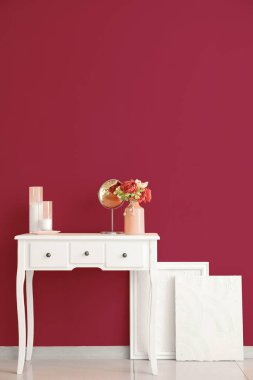 Çiçekli vazo, ayna ve mumlar pembe duvarın yanında.