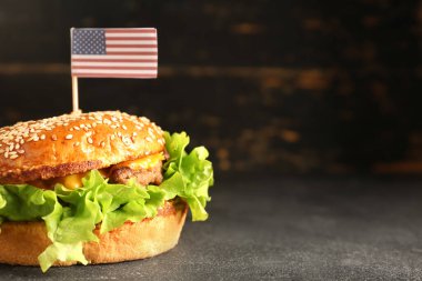 Koyu arkaplanda Anma Günü kutlamaları için kağıt Amerikan bayrağıyla lezzetli bir burger.