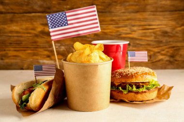 Lezzetli burger, patates cipsi, sosisli sandviç ve bir bardak içki, tahta arka planda. Anma Günü kutlaması