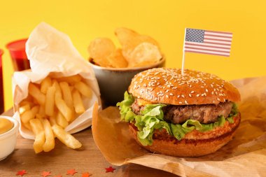 Tahta tahtada lezzetli hamburger, patates kızartması ve patates cipsi, yakın plan. Anma Günü kutlaması