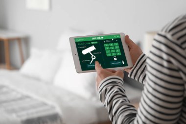 Genç adam yatak odasında akıllı ev güvenlik sistemi kontrol paneli kullanıyor.