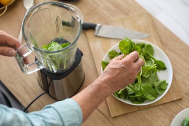 Olgun adam mutfakta ıspanaklı smoothie yapıyor, yakın plan.