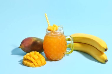 Mason kavanozu taze mango smoothie ve muzlar mavi arka planda