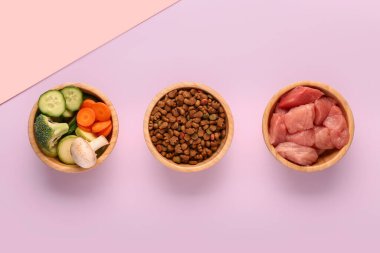 İçinde kuru hayvan mamaları, çiğ et ve pembe arka planda doğal ürünler olan kaseler.