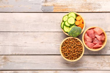 Kuru hayvan mamasıyla dolu kaseler, çiğ et ve hafif ahşap arka planda doğal ürünler.