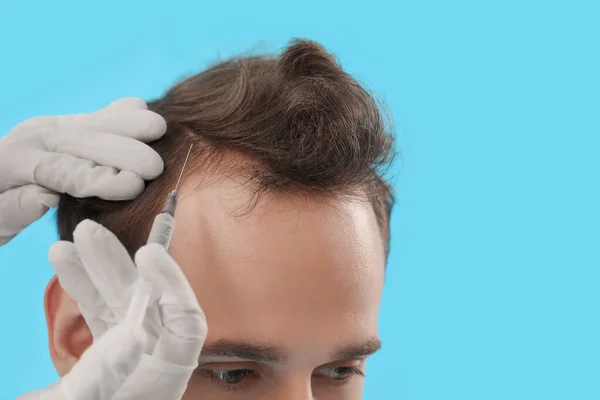 Young man receiving injection for hair growth on blue background, closeup