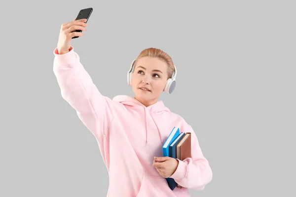 Νεαρή Γυναίκα Ακουστικά Βιβλία Που Βγάζουν Selfie Γκρι Φόντο — Φωτογραφία Αρχείου