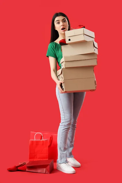Female seller with shoe boxes and shopping bags on red background