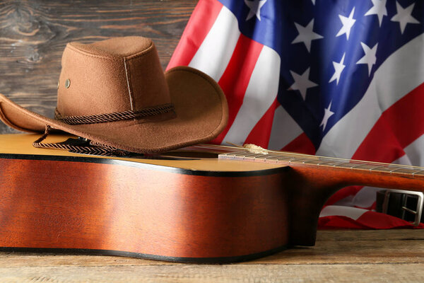 Cowboy hat, guitar and flag of USA on wooden background