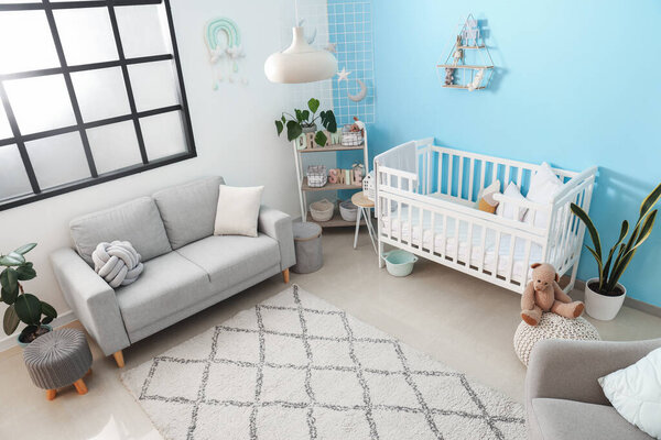 Interior of stylish bedroom with baby crib, sofa and shelving unit