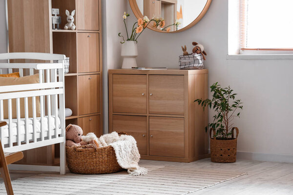 Interior of light bedroom with baby crib and drawers