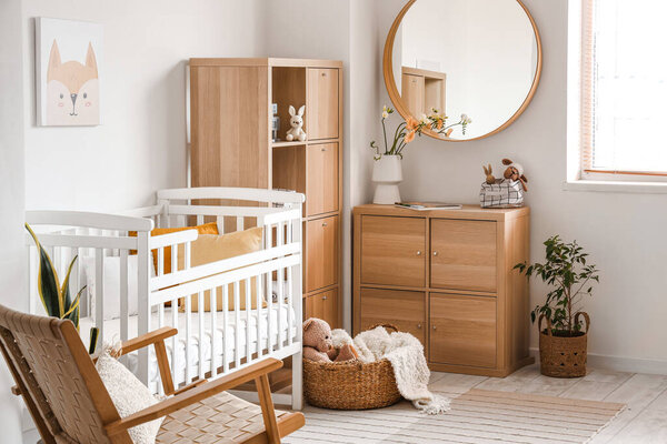 Interior of light bedroom with baby crib, drawers and mirror