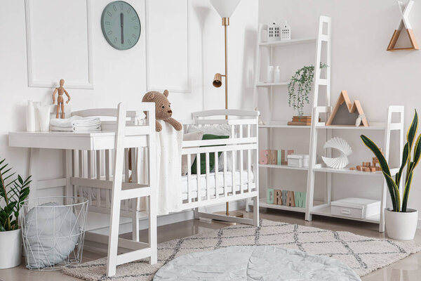 Interior of light bedroom with baby crib, changing table and shelving unit