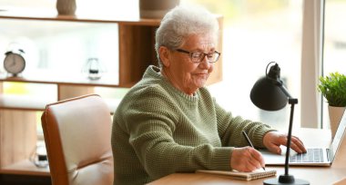 Dizüstü bilgisayar ve defterle çalışan kıdemli bir kadın.