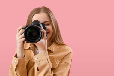 Pembe arka planda profesyonel kameralı genç bayan fotoğrafçı, yakın plan.