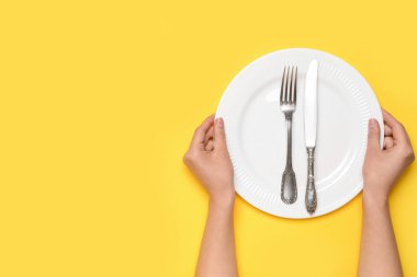 Sarı arka planda boş tabak ve çatal bıçak takımı olan kadın elleri.