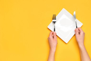 Turuncu arka planda boş tabak ve çatal bıçak takımı olan kadın elleri.
