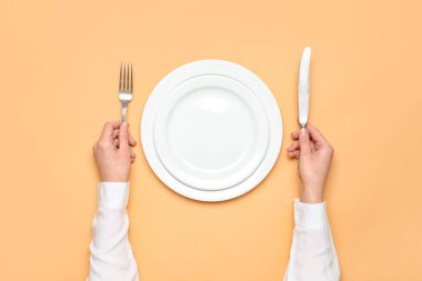Bej arka planda boş tabak ve çatal bıçak takımı olan kadın elleri.