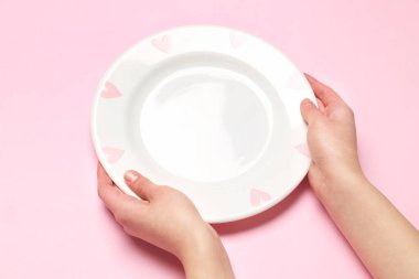 Pembe arka planda boş tabağı olan kadın elleri