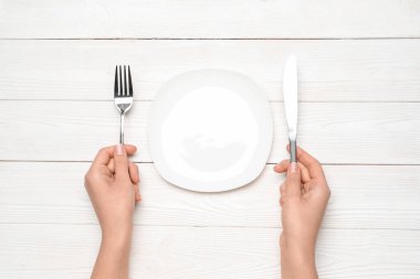 Beyaz ahşap arka planda boş tabak ve çatal bıçak takımı olan kadın elleri.