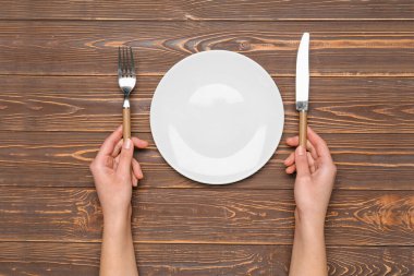 Kahverengi ahşap arka planda boş tabak ve çatal bıçak takımı olan kadın elleri.