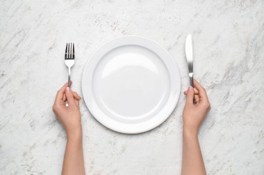 Beyaz grunge arka planda boş tabak ve çatal bıçak takımı olan kadın elleri