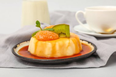 Lezzetli puding, kivi ve gri arkaplanda karamel şurubuyla kaplı mandalinalarla dolu bir tabak.