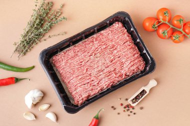 İçinde taze et, domates, kekik ve bej arka planda sarımsak olan plastik paket.