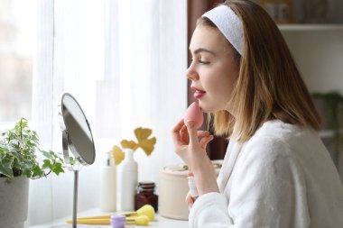 Evde süngerle makyaj yapan genç bir kadın.