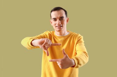 Genç adam yeşil arka planda elleri ile çerçeve yapıyor.