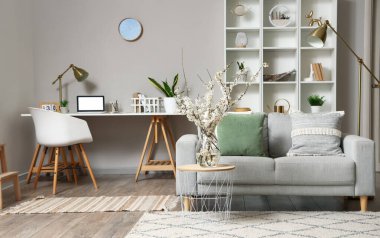 Oturma odasının içinde gri kanepe ve sehpanın üzerinde çiçek açan ağaç dalları var.