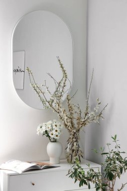 Kasımpatı çiçekli vazolar ve çiçek açan ağaç dalları yatak odasındaki çekmecelerin üzerinde.