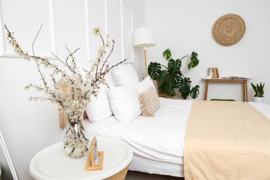 Çiçek açan ağaç dalları olan vazo yatak odasındaki komodinin yanında.