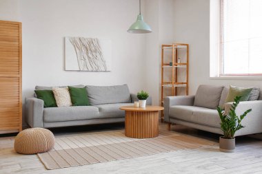 Aydınlık oturma odasının içinde gri kanepeler ve kahve masasının üzerinde bitkiler var.