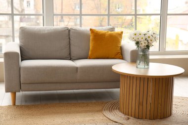 Gri kanepesi ve büyük pencerenin yanında ahşap sehpası olan aydınlık oturma odasının içinde.