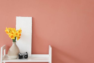 Kahverengi duvarın yanındaki raflarda çiçek açan vazo ve fotoğraf makinesi.
