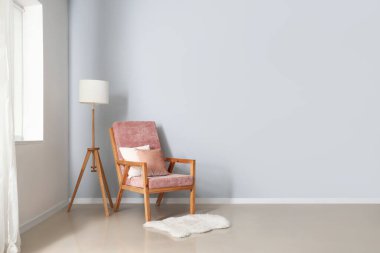 Gri duvarın yanında yastıklı, lambalı ve kürklü rahat pembe koltuk.