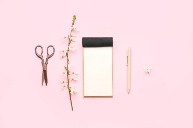Pembe arka planda çiçek açan ağaç dalı, defter, kalem ve makas bileşimi