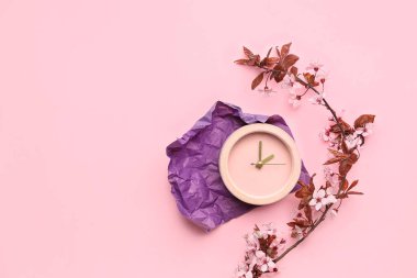 Çiçekli ağaç dalları ve pembe arka planda çalar saat.